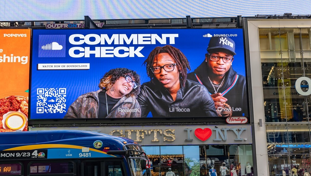Large Times Square billboard with a bright blue SoundCloud ad reads "COMMENT CHECK" above portraits of RealestK, Lil Tecca, and Chow Lee. A QR code appears on the left beside the text "WATCH NOW ON SOUNDCLOUD" while a city bus passes in front of the "I ♥ NY" gift shop below.