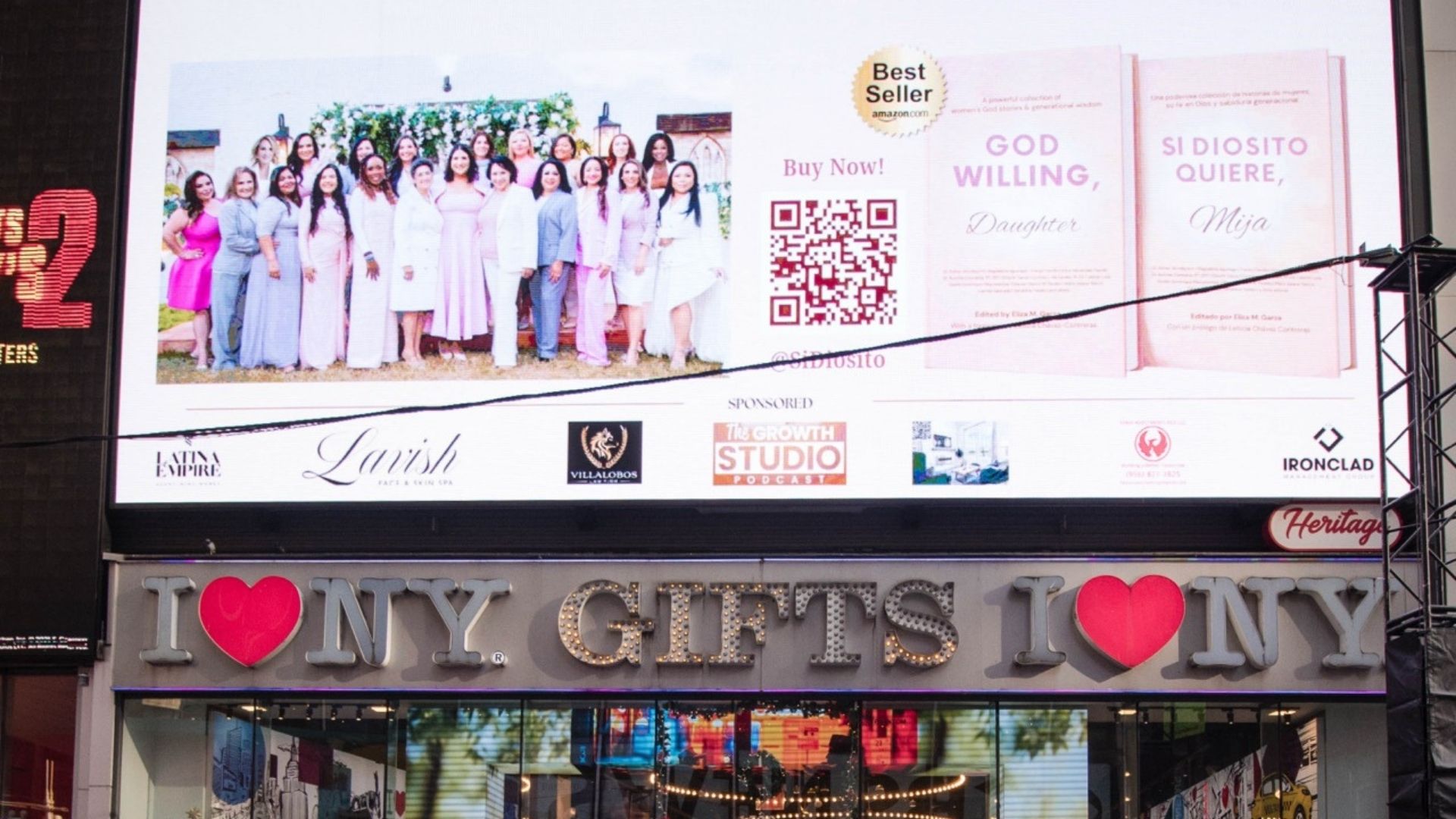 Large Times Square billboard above the "I Love NY Gifts" storefront displays a group photo of women, a QR code, and book covers titled "GOD WILLING, Daughter" and "SI DIOSITO QUIERE, Mija." Smaller sponsor logos appear along the bottom of the ad, including "LATINA EMPIRE," "Lavish," "VILLALOBOS," "The Growth Studio Podcast," and "IRONCLAD."