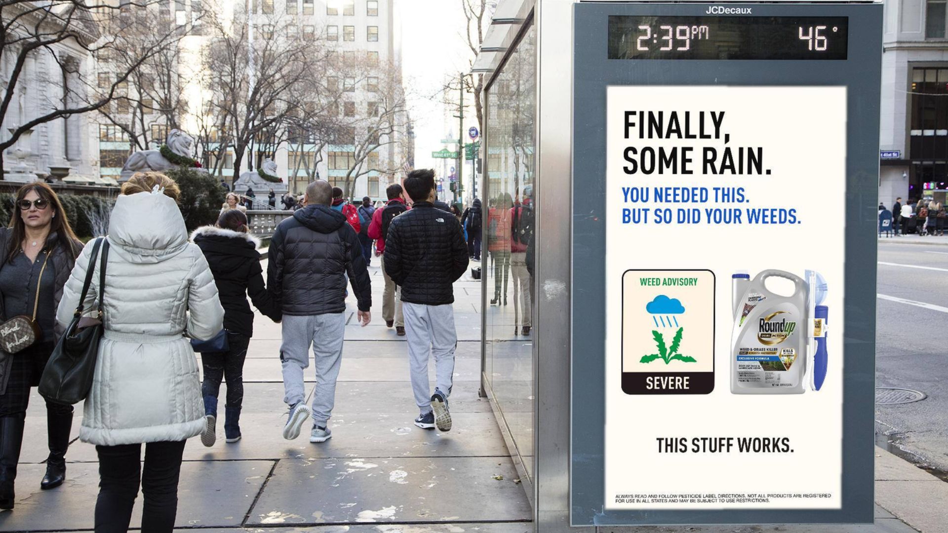 Sidewalk digital billboard shows a Roundup ad with the text "FINALLY, SOME RAIN. YOU NEEDED THIS. BUT SO DID YOUR WEEDS." beside a "WEED ADVISORY SEVERE" icon and Roundup products. A display above the screen reads "2:39 PM" and "46°" while pedestrians in winter coats walk past on a city sidewalk.